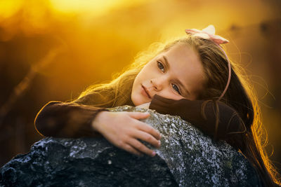 Close-up of sad girl leaning on rock during sunset