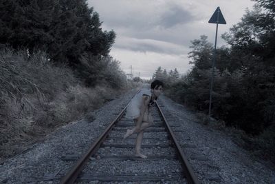 Portrait of mature woman standing on railroad track against cloudy sky at dusk