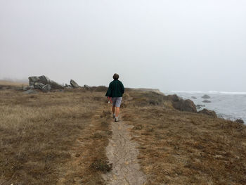 Rear view full length of woman walking on cliff against sky