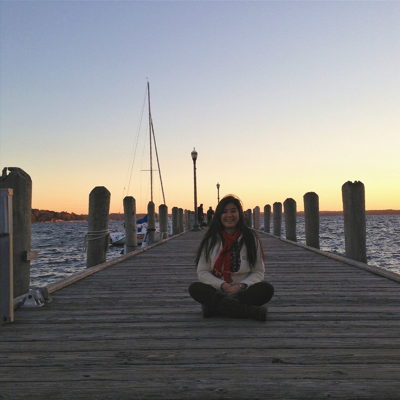 clear sky, lifestyles, sea, water, leisure activity, copy space, pier, sitting, built structure, full length, rear view, standing, casual clothing, person, sunset, railing, architecture, young adult