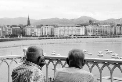 Rear view of people sitting on railing against cityscape