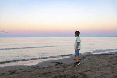 Lonely kid watching the ocean at sunset