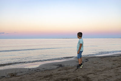 Full length of man standing on beach against sky during sunset