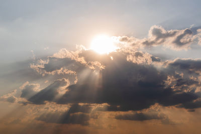 Low angle view of sunlight streaming through clouds