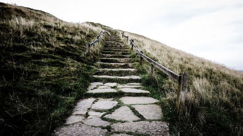 Staircase on grassy hill against sky