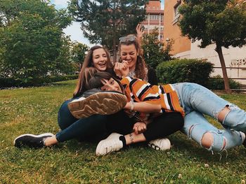 Happy friends sitting on grass against trees