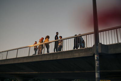 Low angle view of friends standing on bridge against sky