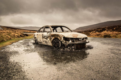 Abandoned car on road against sky during rainy season