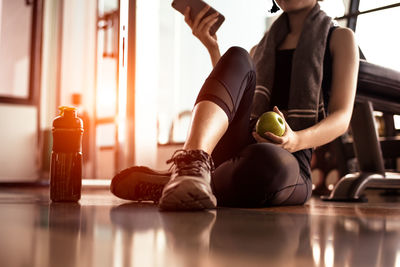 Low section of woman sitting with apple in gym