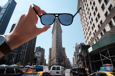 Cropped hand with sunglasses against cars and flatiron building in city