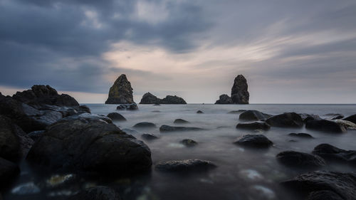 Rocks in sea against sky during sunset