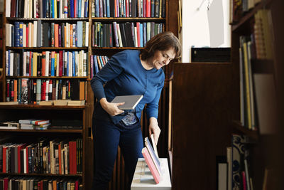 Full length of woman reading book while standing in library