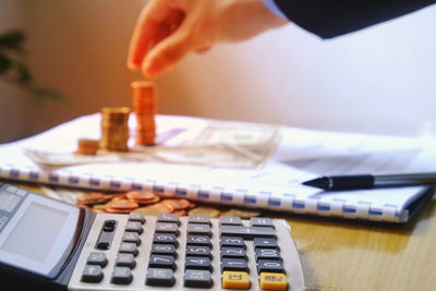 Cropped hand of businessman stacking coins by calculator