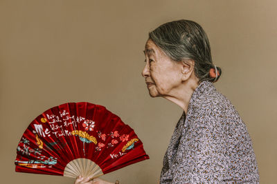 Side view of woman looking away against beige background