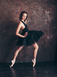 Portrait of young woman dancing against wall in dance studio
