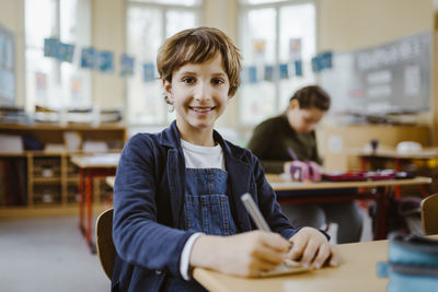 Portrait of smiling schoolboy sitting at desk in classroom
