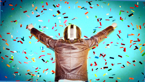 Confetti falling on biker with arms raised standing against turquoise wall