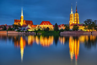 Illuminated building by lake against sky