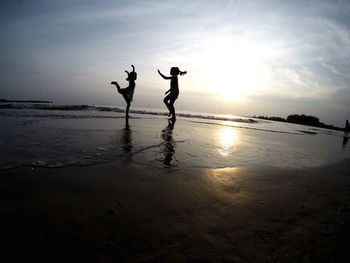 Silhouette people at beach against sky during sunset