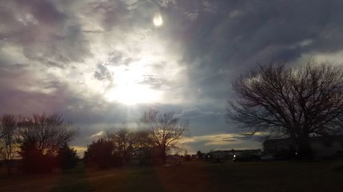 Bare trees on landscape against sky during sunset