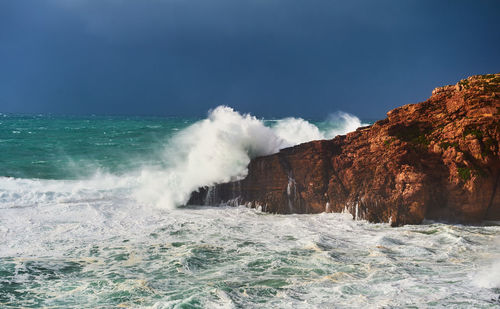 Waves splashing on rocks against sky