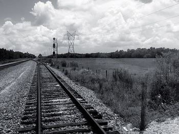 Railroad track by field against cloudy sky