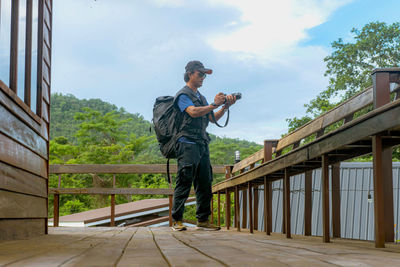 Young photographer holding digital camera standing on wooden resort, lifestyle concept