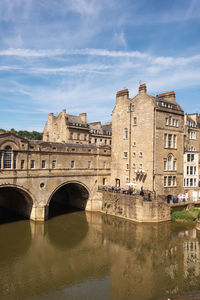 Arch bridge over river by buildings against sky