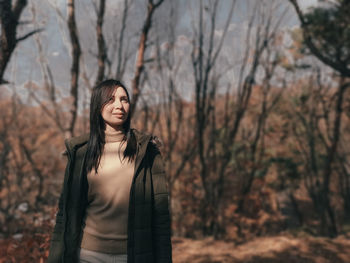 Woman standing by bare tree in forest