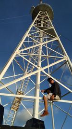 Low angle view of man standing on metallic structure against blue sky