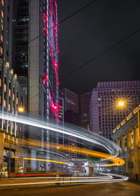 Light trails on road against illuminated buildings in city at night