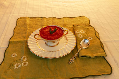 Tomato soup in a white and gold bowl on an embroidered green placemat.