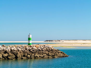 Lighthouse by sea against clear sky