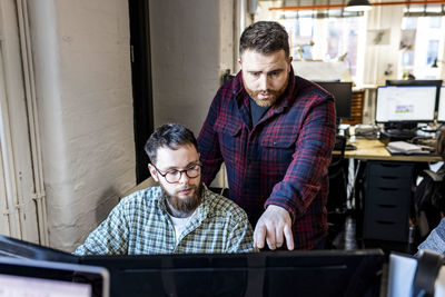 Businessman having discussion with colleague over computer in office