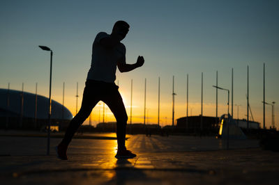 Side view of silhouette woman walking on street against sky during sunset