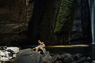 People sitting on rock by trees in forest