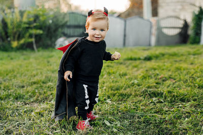 A charming kid in a devil costume and a raincoat sneaks around the garden. halloween concept