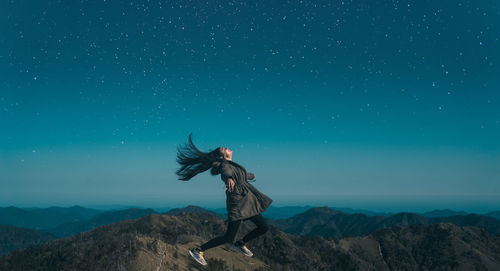 Man with arms raised against blue sky at night