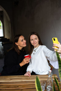 Two women friends have fun outdoors in cafe and take a selfie on a smartphone