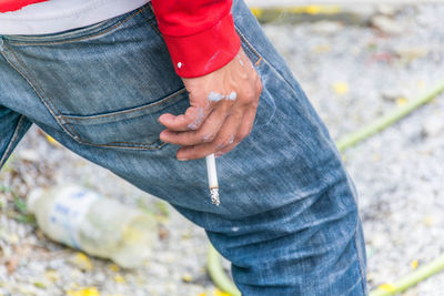 Midsection of man holding burnt cigarette outdoors