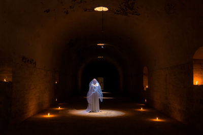 Lady in white bride dress like an angel at a religious mass with burning torches in the dungeon