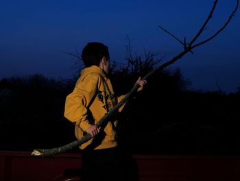 Boy carrying stick while walking on field at dusk