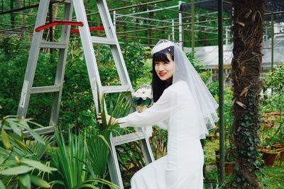 Portrait of bride climbing on ladder against trees