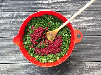 Directly above shot of chopped berries on green vegetables in bowl with spatula