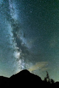 Low angle view of galaxy over silhouette mountain at night