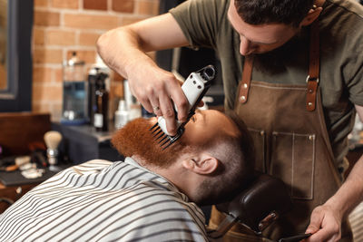 Barber trimming beard of customer