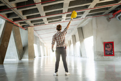 Rear view full length of engineer holding hardhat while standing at construction site