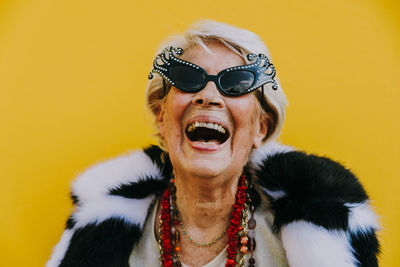 Portrait of senior woman laughing while standing against yellow background