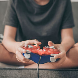 Low section of boy playing video game while sitting on sofa in living room at home