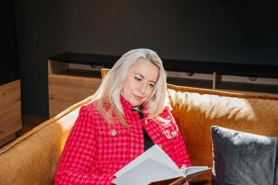 Mature lady engrossed in a novel, relaxed on a mustard couch